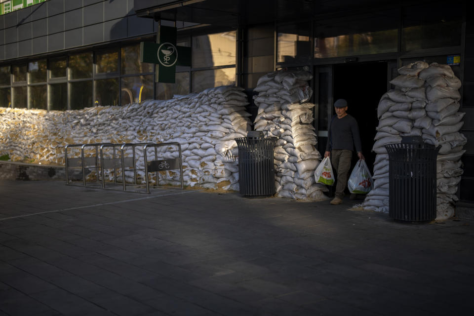 A man carrying bags leaves a supermarket protected by sandbags in the center of Mykolaiv, Monday, Oct. 24, 2022. (AP Photo/Emilio Morenatti)