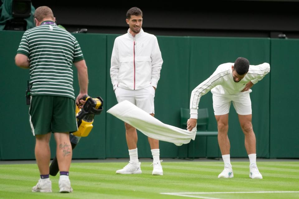 Djokovic attempts to dry the grass with a towel (Copyright 2023 The Associated Press. All rights reserved)