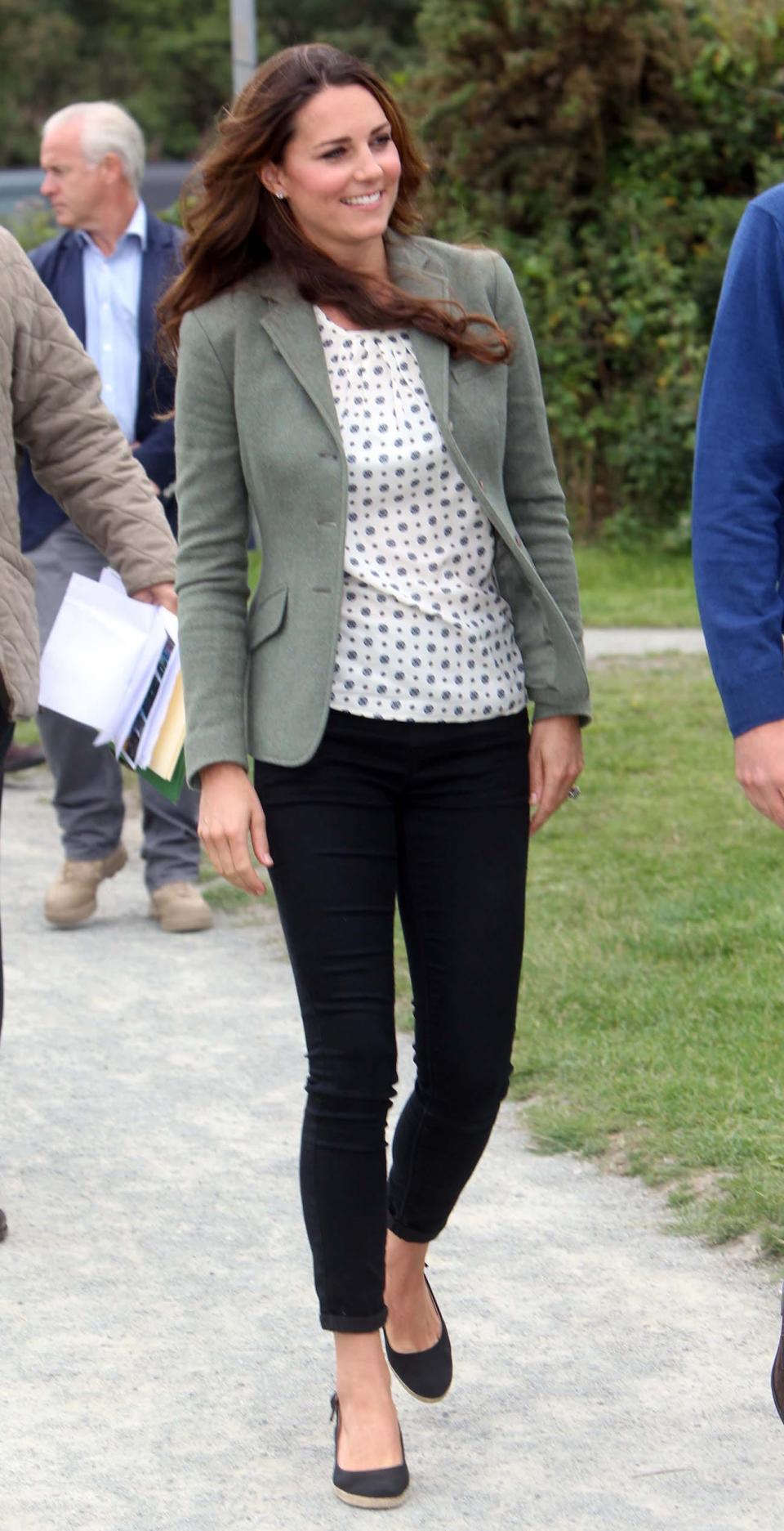 Kate Middleton wears a green blazer, a patterned white shirt, and black pants.