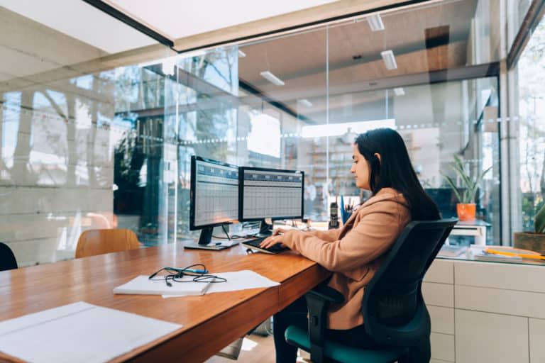 A worker uses a double monitor computer screen in an office.