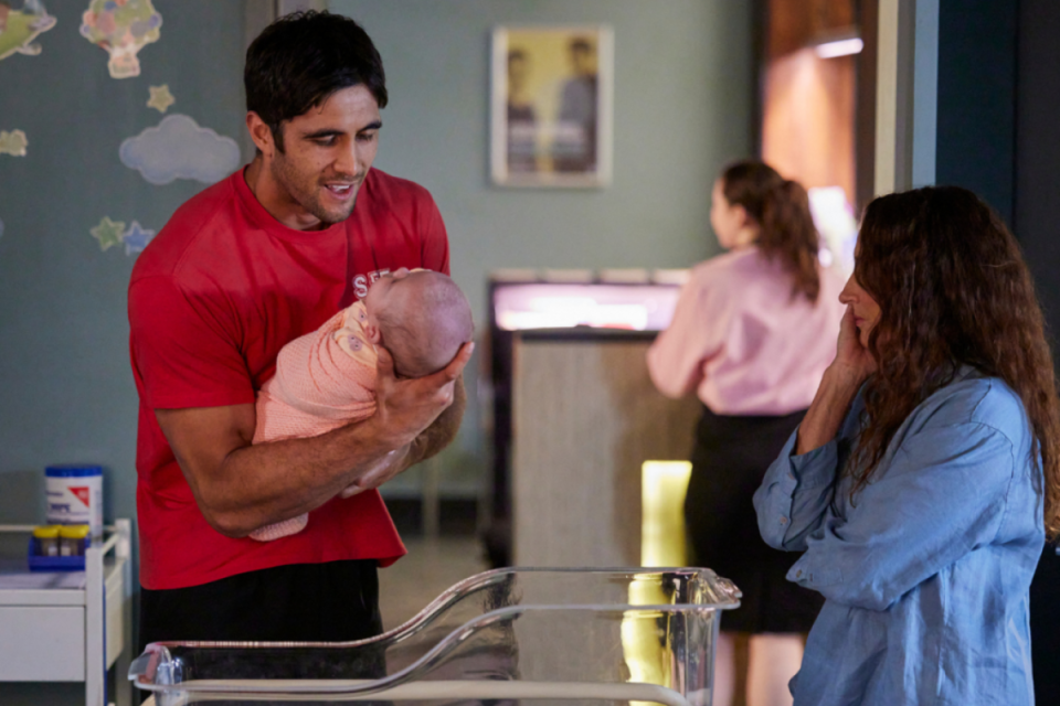 Tane Parata holding a baby in the hospital with Roo Stewart watching.