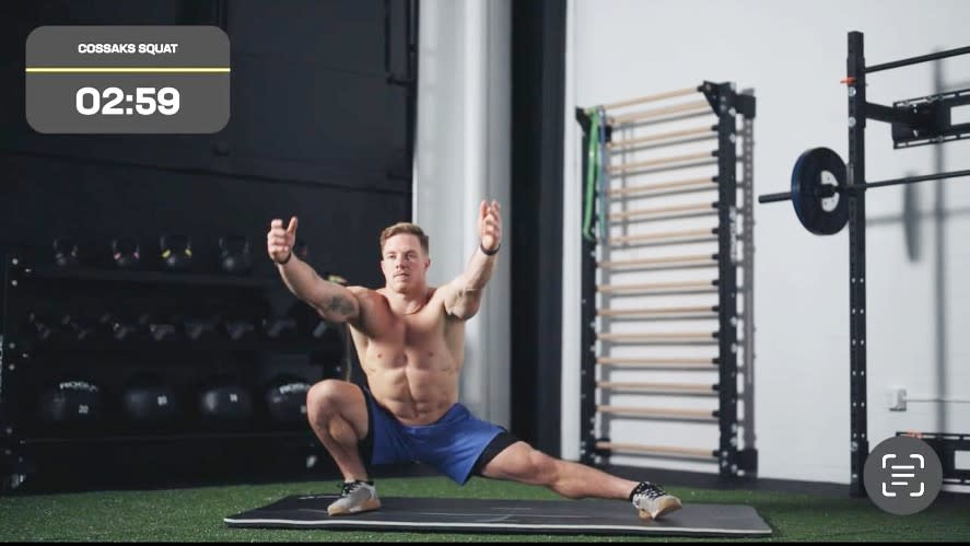 Noah performing a Cossack squat with arms outstretched and lunging to the right hand side