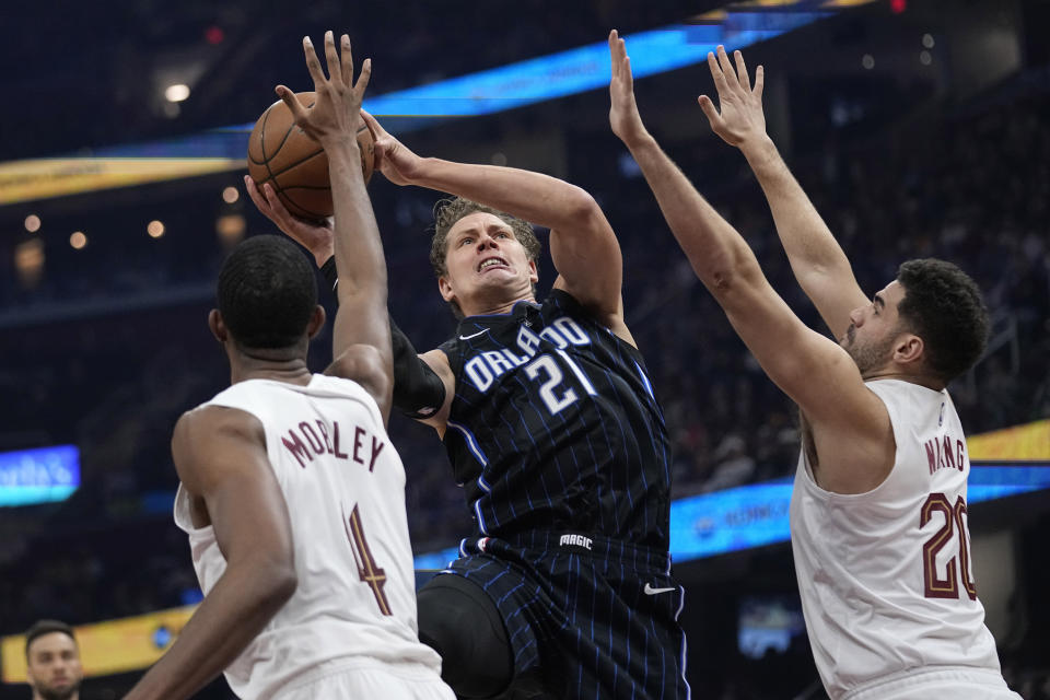 Orlando Magic center Moritz Wagner (21) shoots between Cleveland Cavaliers forward Evan Mobley (4) and forward Georges Niang (20) during the first half of an NBA basketball game Thursday, Feb. 22, 2024, in Cleveland. (AP Photo/Sue Ogrocki)