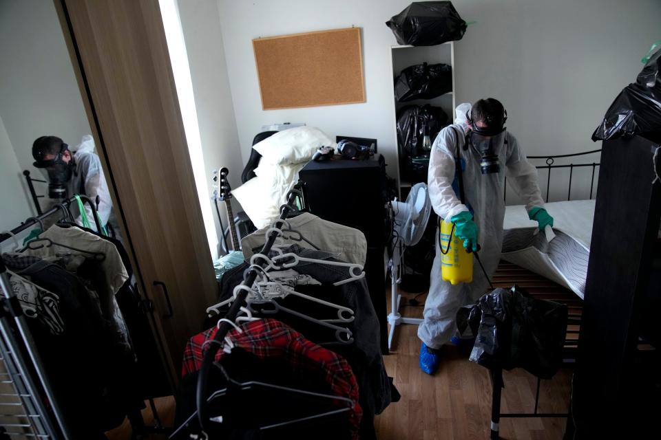 A pest control technician sprays insecticide under a mattress.