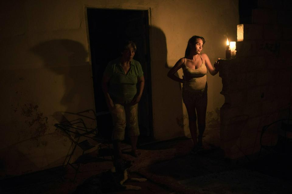 In this May 15, 2019 photo, Jennifer Vejar is illuminated by a torch known in Maracaibo as a "Mechurrio" during a black out in Maracaibo, Venezuela. Critics blame Venezuela’s crisis on the socialist “revolution” President Hugo Chávez launched 20 years ago, saying he allowed corrupt officials to loot the national coffers while public infrastructure fell into disrepair. (AP Photo/Rodrigo Abd)