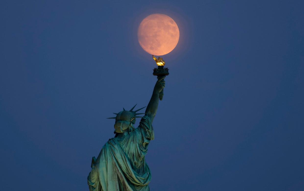 The moon pictured in New York City, with the Statue of Liberty in the foreground