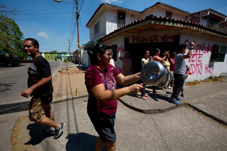 In this photo taken on Saturday, March 15, 2014. A resident hits a pot near a graffiti that reads in Spanish "Collective go, damn" during an opposition protest at Isabelica neighborhood outside Valencia , Venezuela. The people of the poor district of La Isabelica were made to pay for taking to the streets in anti-government protests. More than a dozen masked men on motorcycles roared through, shooting up a barricade and killing a university student and a 42-year-old man painting his house. (AP Photo/Fernando Llano)