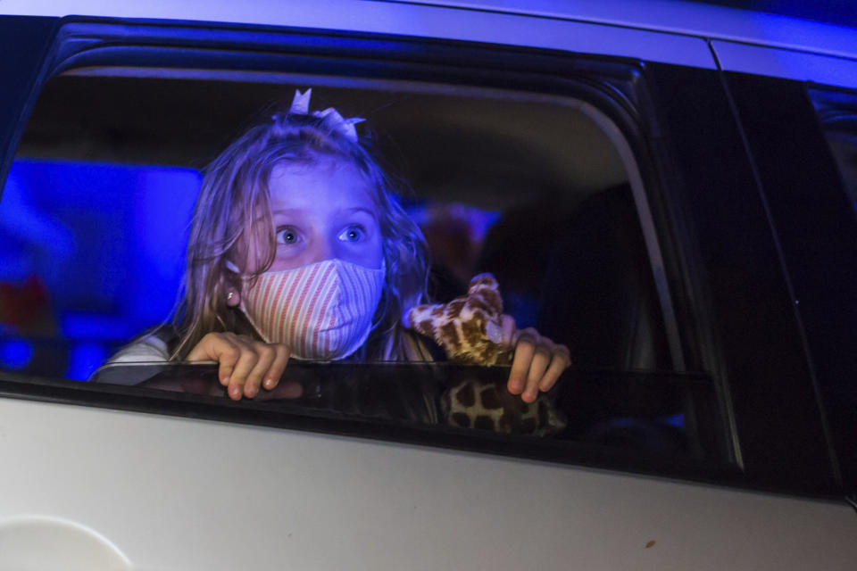 Una niña con mascarilla contempla un espectáculo desde el interior de un auto en el parque de diversiones con temática de terror Hopi Hari en Sao Paulo, Brasil, 4 de septiembre de 2020. Debido a las restricciones del coronavirus, el parque creó un tour en auto que permite disfrutar la experiencia desde el auto. (AP Foto/Carla Carniel)