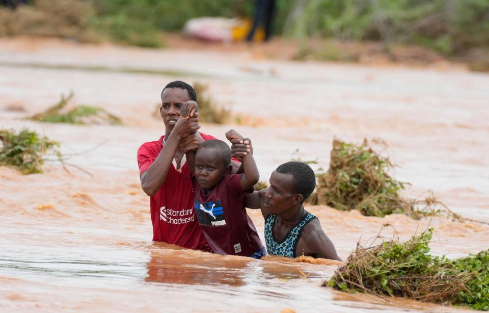 Residents help a young child while trying to cross a road damaged by El Niño rains in Tula, Tana River county in Kenya on Saturday, Nov. 25, 2023.