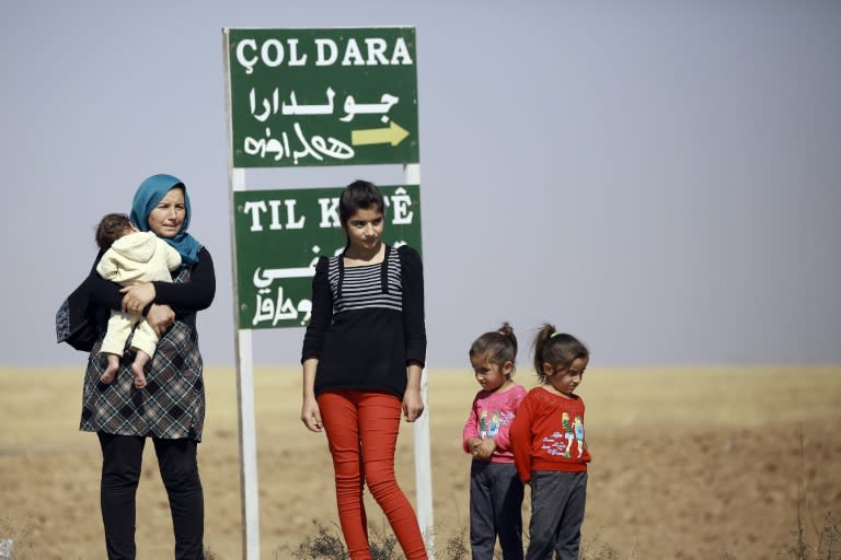 A Kurdish woman and her children stand by a sign for the village of Joldara (meaning plain covered in trees) and known as Shajra in Arabic, near the northeastern Syrian city of Qamishli on October 3, 2016