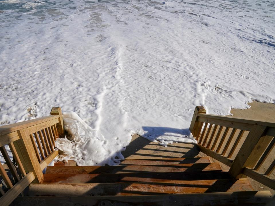 Atlantic Ocean water pushes sand over the deck steps of a beachfront house on Seagull Street in December 2022.