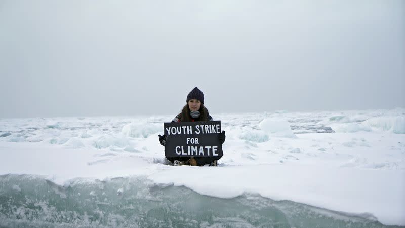 Environmental activist and campaigner Mya-Rose Craig holds a cardboard sign reading “youth strike for climate” in the middle of the Arctic Ocean