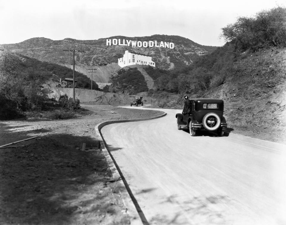 A sign advertises the opening of the Hollywoodland housing development in the hills on Mulholland Drive overlooking Los Angeles, Hollywood, Los Angeles, California, circa 1924. The white building below the sign is the Kanst Art Gallery, which opened on April 1, 1924.