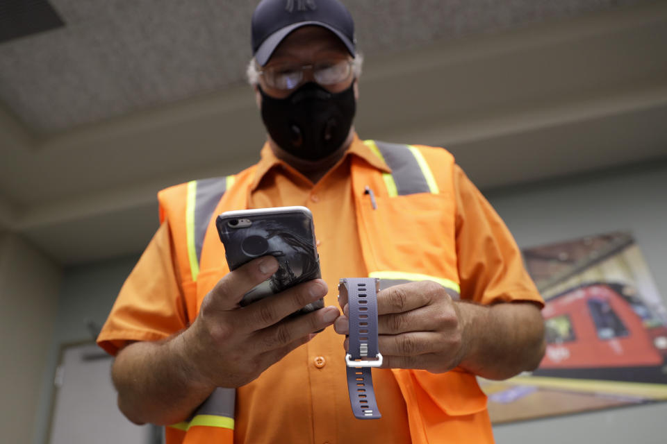 San Diego Metropolitan Transit System worker John Freeland takes a look at a new Fitbit device Thursday, July 9, 2020, in San Diego. The device is part of a Scripps Research “DETECT” study to monitor a person's heart rate and allow participants to record symptoms like fever or coughing to share with scientists, in an attempt to see if they can spot COVID-19. (AP Photo/Gregory Bull)