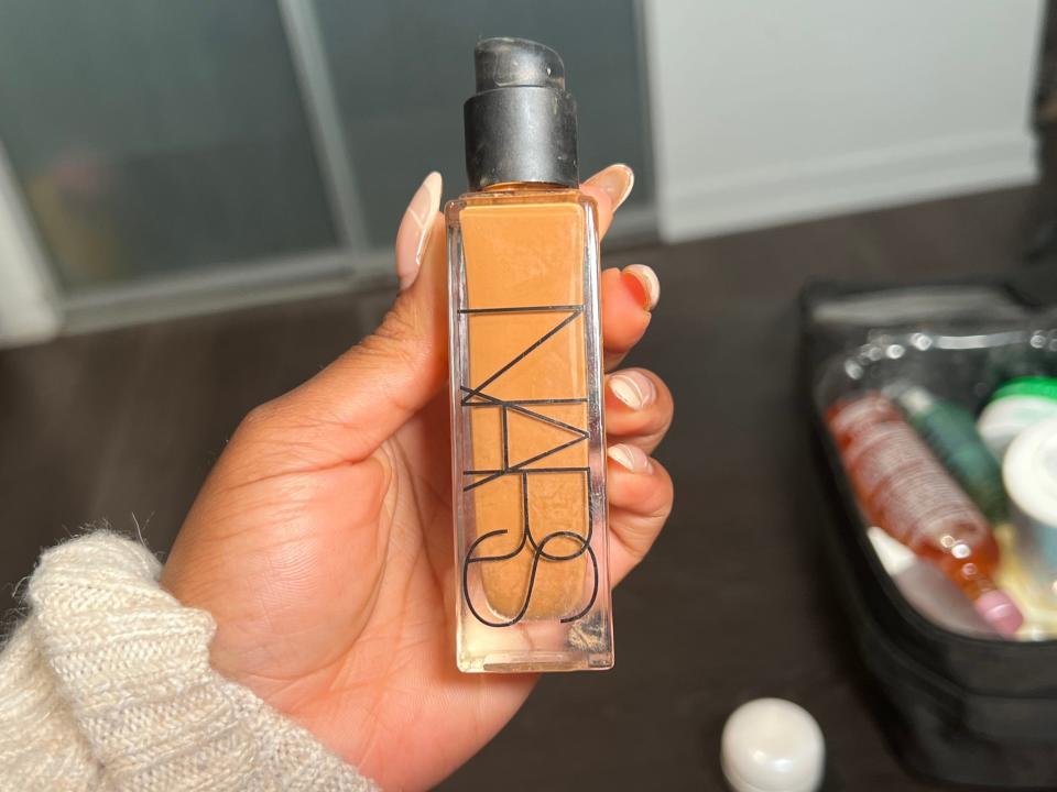 The writer holds a glass bottle of foundation with "Nars" text on it