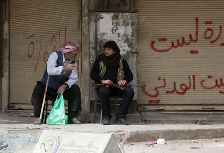 A man gestures as he sits next to a Turkish-backed Free Syrian Army fighter in the center of Afrin, Syria March 24, 2018. REUTERS/Khalil Ashawi