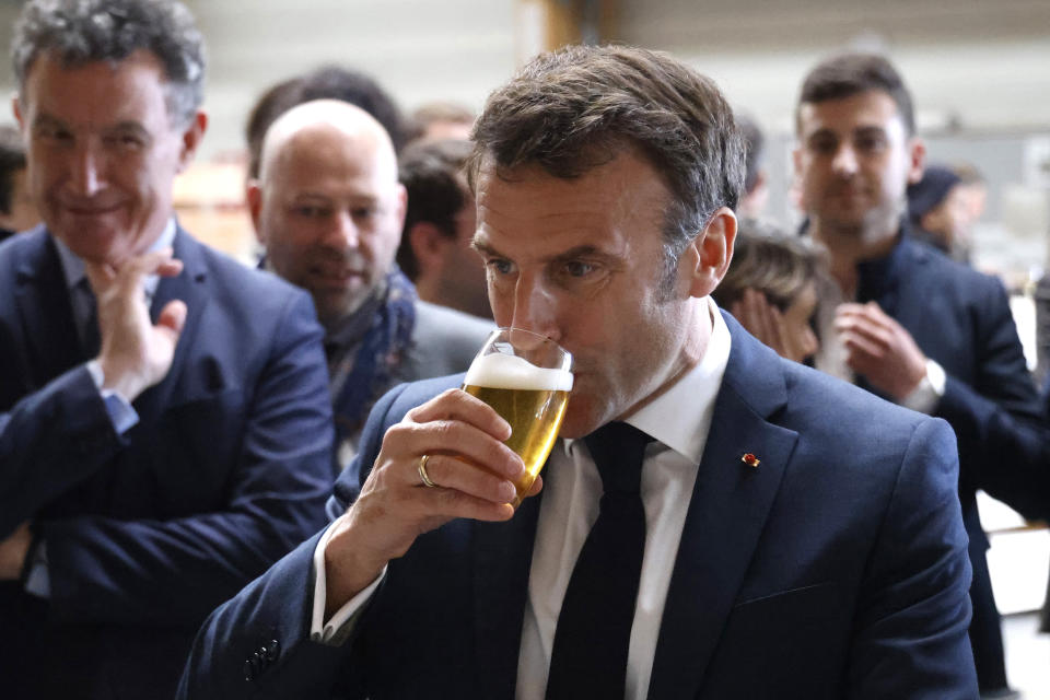 French President Emmanuel Macron drinks a beer during a visit to Mathis, a company specialized in large wooden buildings, in Muttersholtz, eastern France, Wednesday, April 19, 2023. (Ludovic Marin, Pool via AP)