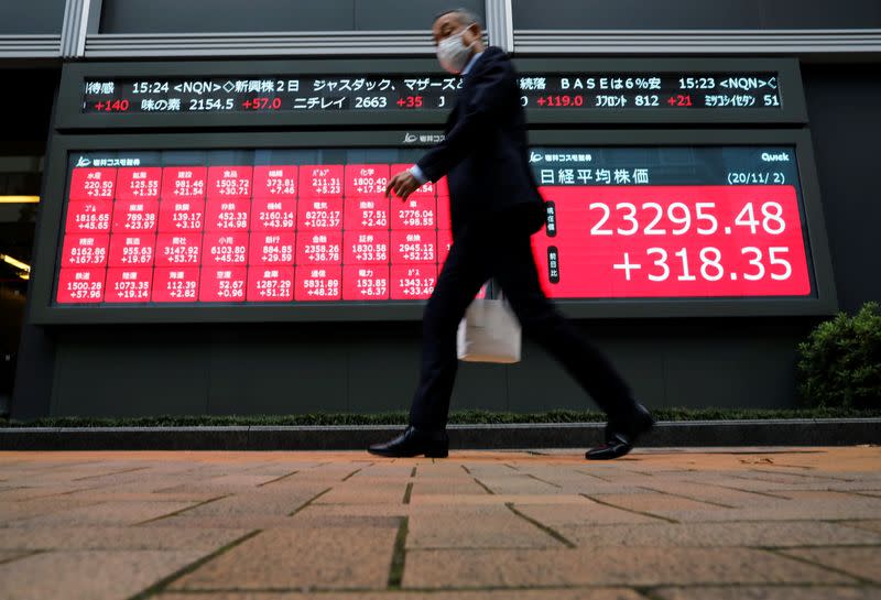 FILE PHOTO: A man wearing a protective face mask walks past a stock quotation board outside a brokerage, amid the coronavirus disease (COVID-19) outbreak, in Tokyo