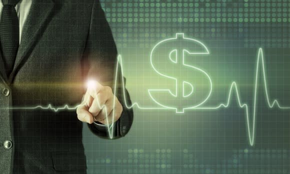 Businessman touching screen displaying heartbeat line and dollar symbol