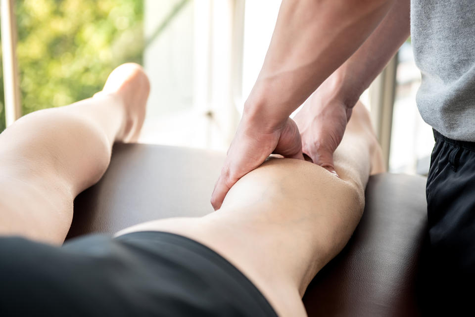 Male therapist giving leg and calf massage to a person lying on a bed.