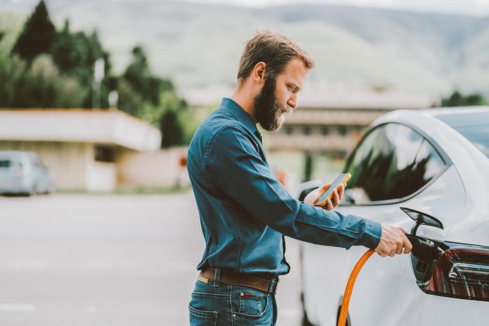 A person charges an EV while holding a smartphone.