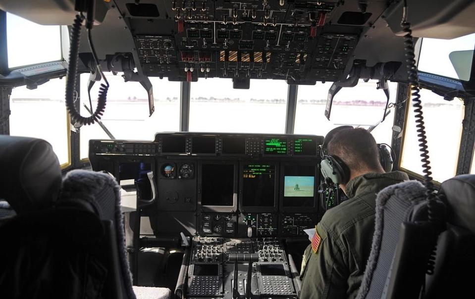 A pilot sits in the cockpit of an MC-130J Commando II surrounded by buttons and levers.