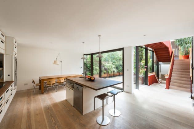 Una cocina a medida y un comedor ocupan todo el ancho de la casa, abriéndose hacia un patio trasero delimitado por un muro.