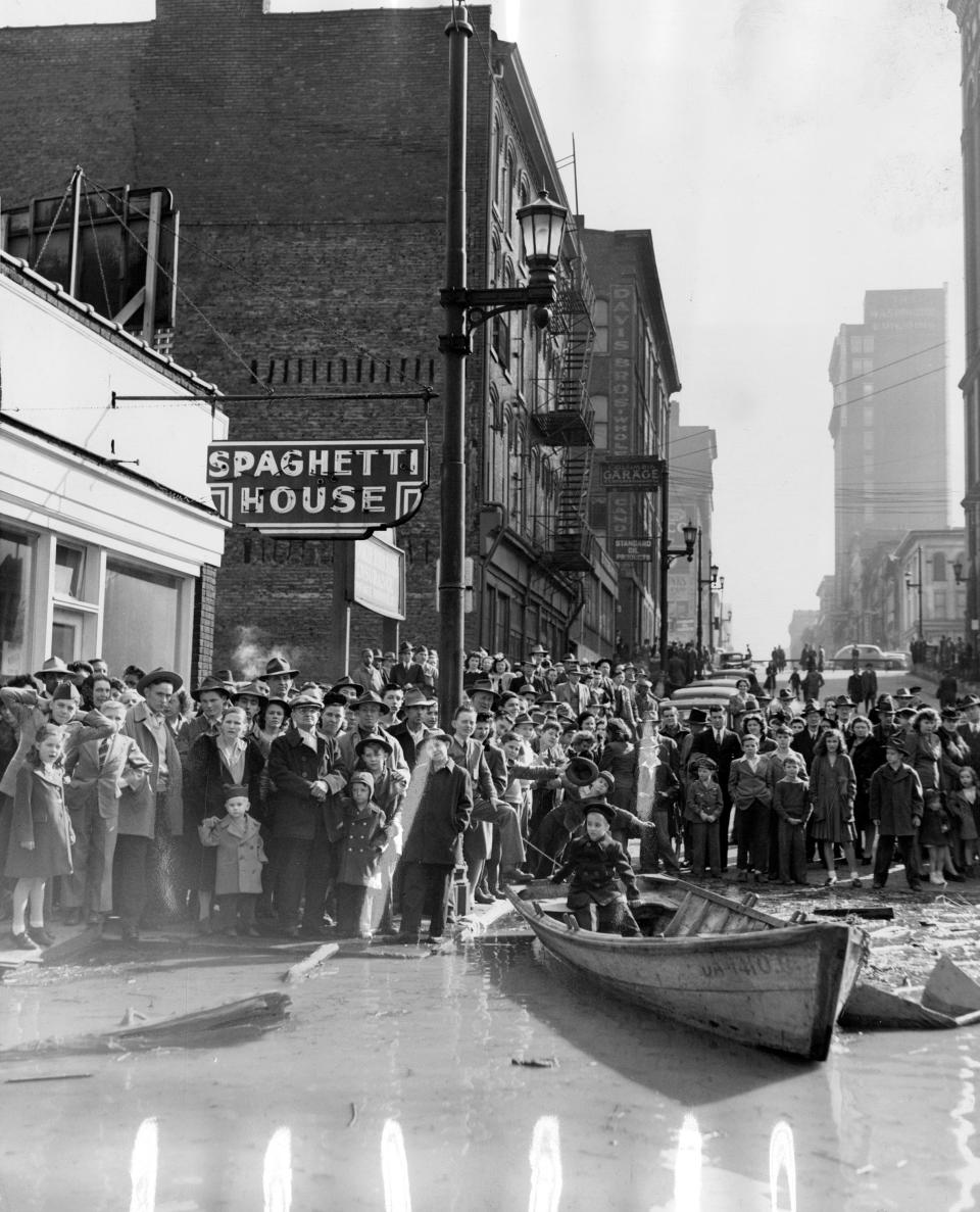 Photo by Al Blunk. March 4, 1945. A warm sun that send the mercury into the 60's yesterday afternoon plus a steadily rising river brought hundreds of people to the water's edge in the downtown area and on the Municipal Bridge. As the photographer passed Fourth Street in a boat, he made this picture. Vehicular traffic, mostly carrying sightseers, caused a mild jam which was soon untabled by bridge police.