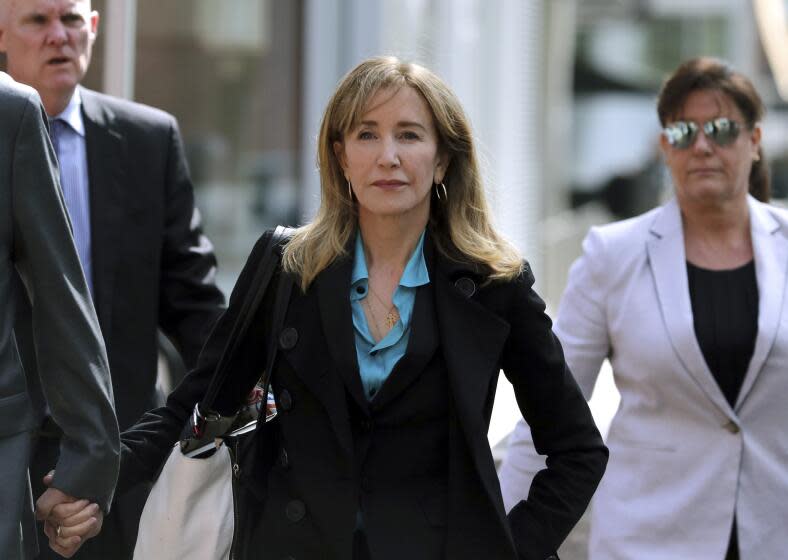 Felicity Huffman in a blue suit shirt and a black suit walking with two people in business attire on either side