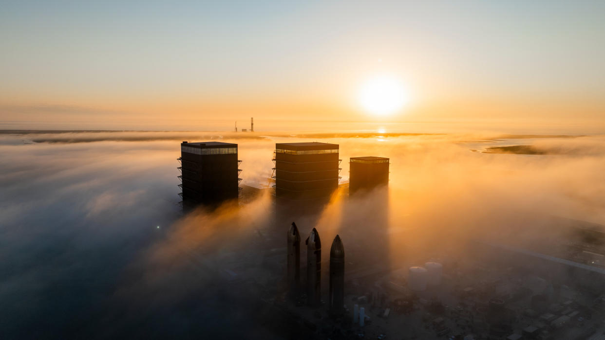  Three rockets rise out of the fog with the sun low on the horizon. 