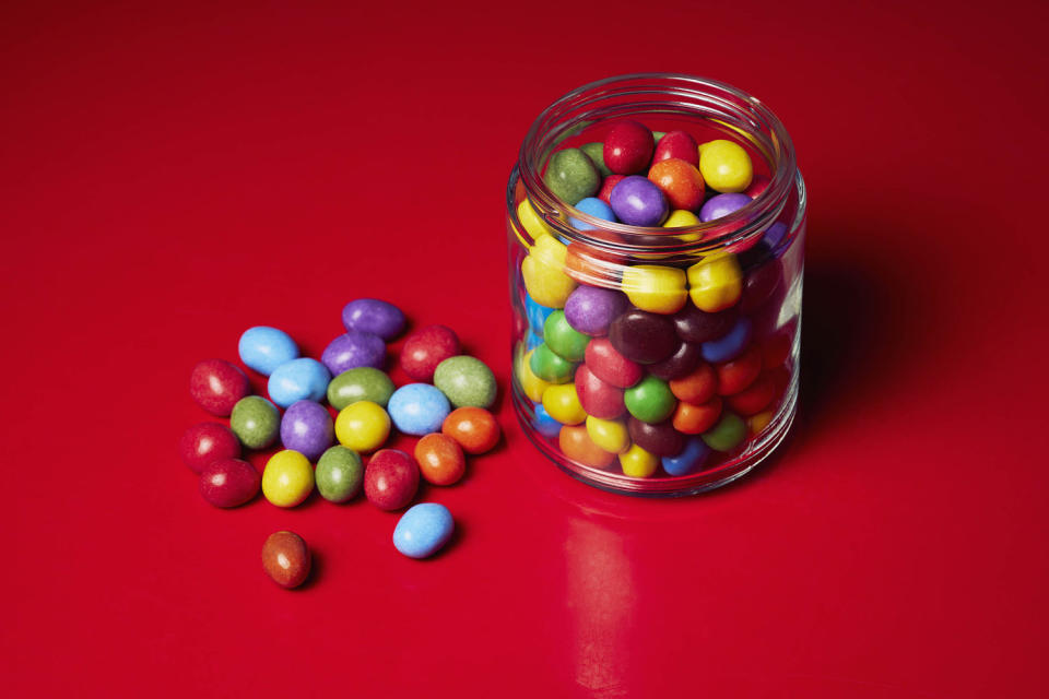 \multicolored candy in glass jar on red background (Norman Posselt / Getty Images / fStop)