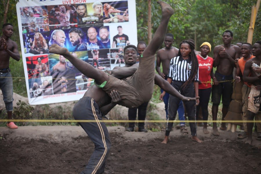 Ugandan youths perform an amateur wrestling tangle in the soft mud in Kampala, Uganda Wednesday, March. 20, 2023. The open-air training sessions, complete with an announcer and a referee, imitate the pro wrestling contests the youth regularly see on television. While a pair tangles inside the ring, made with bamboo poles strung with sisal rope, others standing ringside cheer feints and muscular shows of strength. (AP Photo/Patrick Onen)