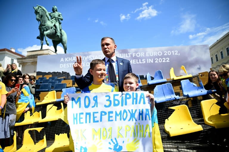 La leyenda del fútbol ucraniano y actual presidente de la federación de ese país Andriy Shevchenko posa junto a unos niños en la exposición temporal de una parte de las gradas del estadio de Kharkiv, destruido por los bombardeos rusos, en Múnich (Alemania) wl 17 de junio de 2024 (Tobias SCHWARZ)