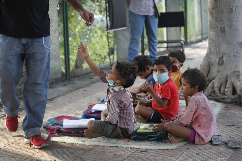 A child takes a pencil during a class conducted by Veena Gupta on a sidewalk in New Delhi, India, Thursday, Sept. 3, 2020. Veena Gupta and her husband are conducting free classes for underprivileged children on a sidewalk in New Delhi. As most schools in India remain shut since late March when the country imposed a nationwide lockdown to curb the spread of COVID-19, many switched to digital learning and taking classes online. (AP Photo/Manish Swarup)