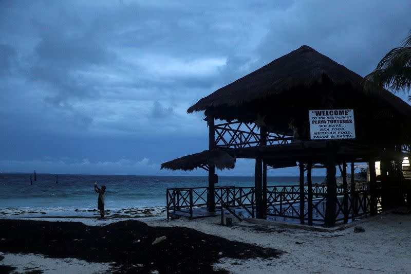 A man takes a video with his phone at a beach as Hurricane Delta approaches Cancun