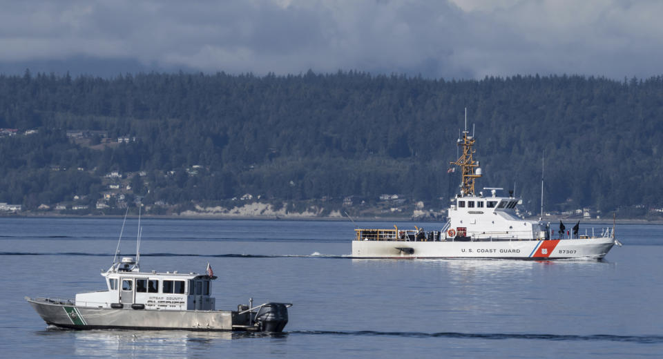 A U.S. Coast Guard boat and Kitsap, Wash., County Sherrif boat search the area, Monday, Sept. 5, 2022, near Freeland, Wash., on Whidbey Island north of Seattle where a chartered floatplane crashed the day before. The plane was carrying 10 people and was en route from Friday Harbor, Wash., to Renton, Wash. (AP Photo/Stephen Brashear)