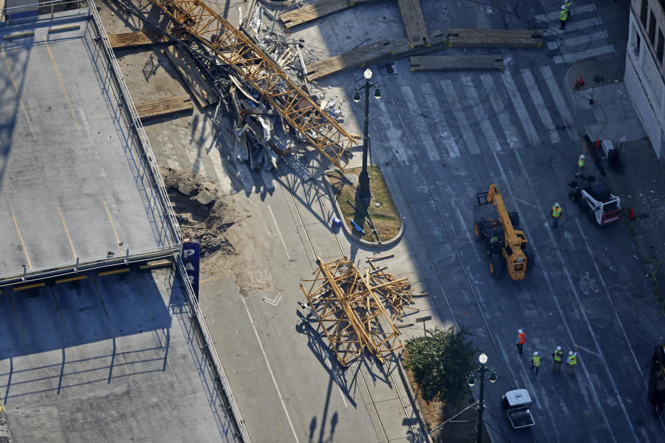 Workers walk near one of the of two large cranes from the Hard Rock Hotel construction collapse after the cranes crashed down, after being detonated for implosion in New Orleans, Sunday, Oct. 20, 2019. (AP Photo/Gerald Herbert)