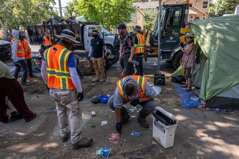 City workers dispose of syringes homeless camper Alicia Peterson, 55, right, who said she was suffering from neuropathy and a wrist injury, looks on at a homeless encampment sweep at 28th and C streets in Sacramento on Wednesday, July 19, 2023. Renée C. Byer/rbyer@sacbee.com