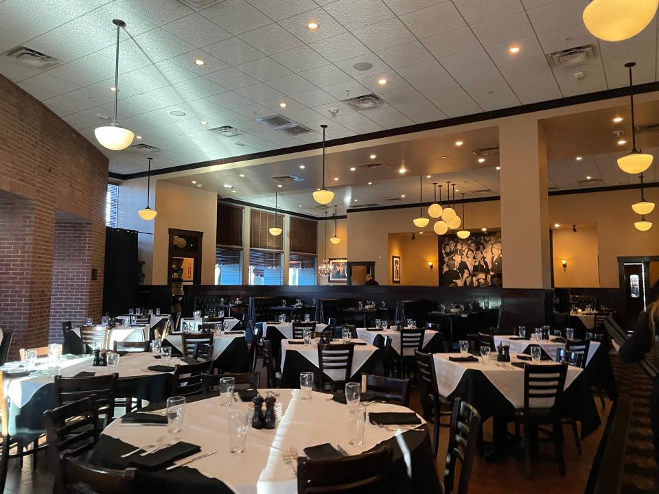 Interior of Maggiano's. The room is filled with dark-brown tables with white tablecloths and chairs. Lights hang from the ceiling