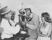 Race car driver Carroll Shelby, of Dallas, Texas, receives his winner's trophy from promotion manager Dave Brandman, after winning the 200-mile International Grand Prix at the Riverside Raceways, California, April 3, 1960. Seen at right is Jan Harrison, the queen of the race. (AP Photo)