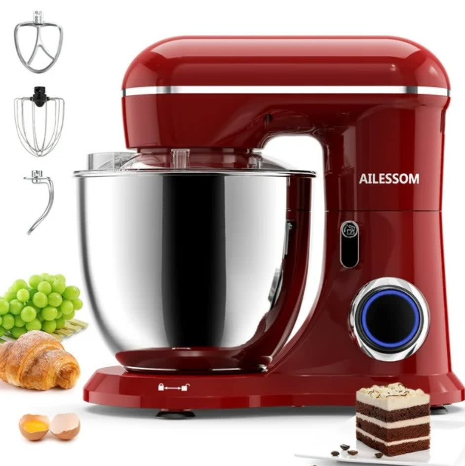Red stand mixer with attached bowl, whisk, and dough hook, alongside ingredients like grapes, eggs, croissant, and cake slice