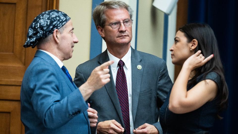 Three members of the United States house of representatives talking amongst themselves in a large hearing room.