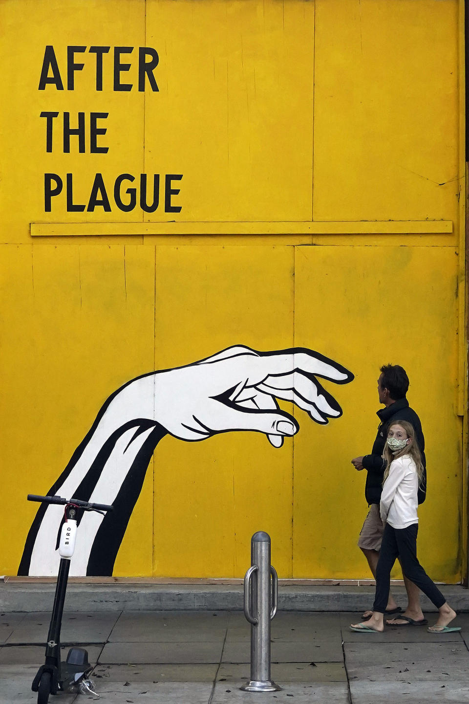 Pedestrians walk past a COVID-19-themed mural outside a boarded up business Monday, Nov. 23, 2020, in Santa Monica, Calif. (AP Photo/Marcio Jose Sanchez)