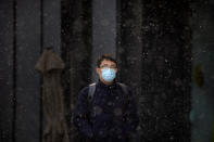 A man wearing a face mask to protect against the spread of the coronavirus walks along a street during a snowy morning in Beijing, Tuesday, Jan. 19, 2021. A Chinese province near Beijing grappling with a spike in coronavirus cases is reinstating tight restrictions on weddings, funerals and other family gatherings, threatening violators with criminal charges. (AP Photo/Mark Schiefelbein)