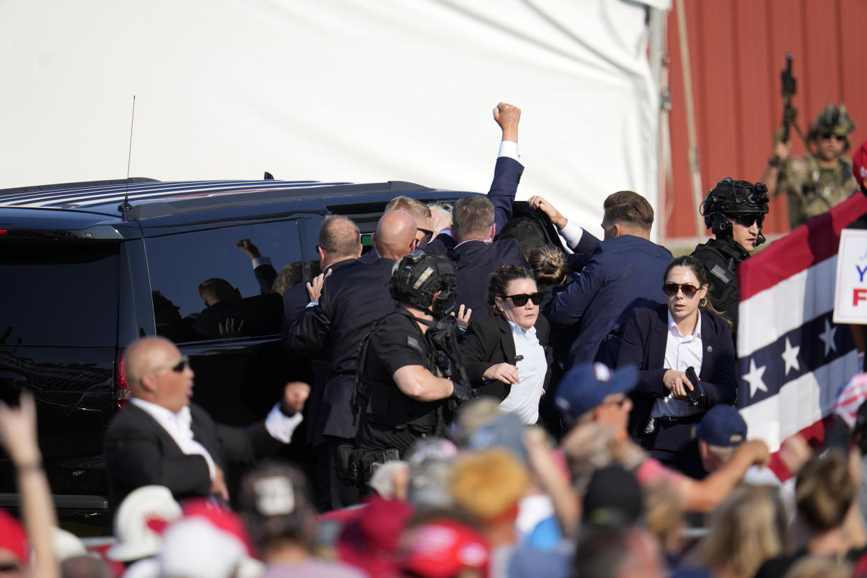 Trump, raising his right fist, is ushered off the stage and into a vehicle.