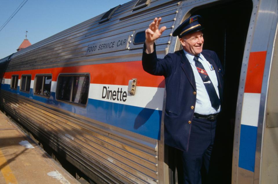 A conductor waving out a door of a train.