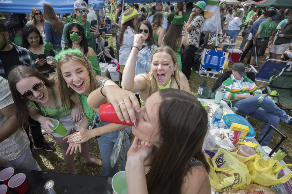 Julie Hensley, al centro, anima subiendo el puño a su amiga Ally Womble, que toma una bebida durante un festejo en una plaza con motivo del Día de San Patricio, el viernes 17 de marzo de 2023, en el centro histórico de Savannah, Georgia. (AP foto/Stephen B. Morton)