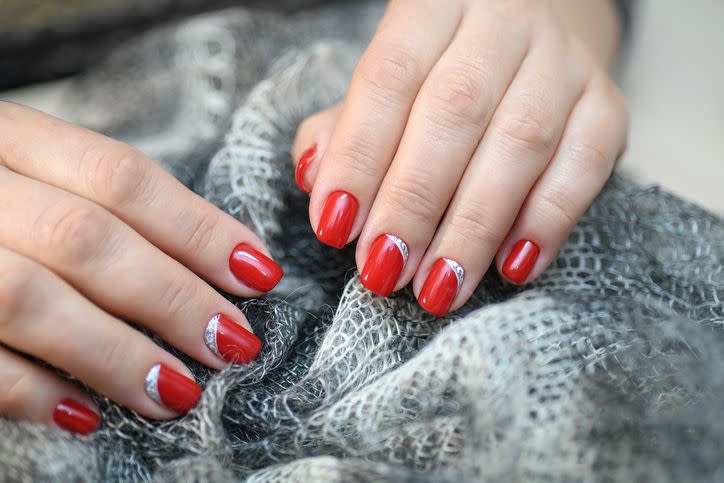 hands with long artificial manicured nails colored with red nail polish and silver gems at the nail bed