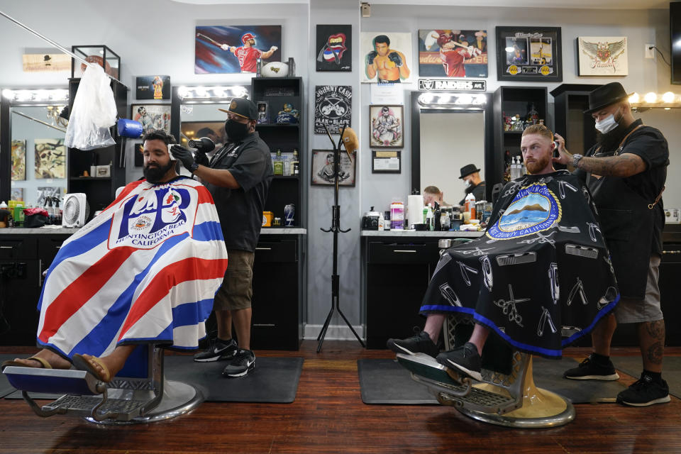 FILE - In this July 15, 2020, file photo, Ricardo Rivera, left, has his hair cut by Anthony Acosta while Braunson McDonald has his hair cut by Luis Lopez, right, owner of Orange County Barbers Parlor in Huntington Beach, Calif. California Gov. Gavin Newsom this week ordered that indoor businesses like salons, barber shops, restaurants, movie theaters, museums and others close due to the spread of COVID-19. (AP Photo/Ashley Landis)