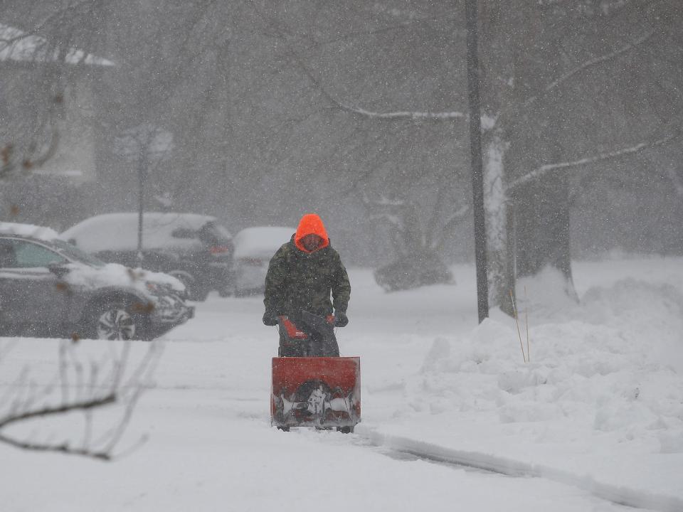 A man uses a snowblower in a blizzard